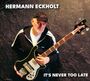 HERMANN ECKHOLT. IT'S NEVER TOO LATE. Ein Mann in Sportjacke mit Gitarre vor schwarzem Hintergrund.