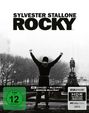 „SYLVESTER STALLONE ROCKY“ in großen Buchstaben. Darunter eine Person mit erhobenen Armen vor einer Allee.