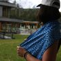Eine Person im Profil trägt eine weiße Kappe, hält ein blau gemustertes Tuch. Im Hintergrund ein modernes Gebäude.