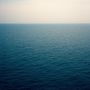 Ein ruhiger, blauer Ozean erstreckt sich bis zum Horizont unter einem hellen, wolkenlosen Himmel.