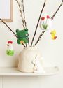 Mehrere Filzdekorationen hängen an Zweigen in einer Vase: Frosch, Ei mit Blume, Huhn, Ente, Hase.