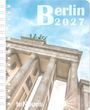 Text: "Berlin 2027". Blick von unten auf das Brandenburger Tor mit strahlendem Himmel. Notizbuch mit Spiralbindung.