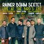 „Rainer Böhm Sextet. Live at the Bird’s Eye. Percy Pursglove, Wanja Slavin, Rainer Böhm, Arne Huber, Jonas Burgwinkel, Domenic Landolf.“ Sechs Männer in dunkler Kleidung stehen vor einer Wand mit tropischem Pflanzenmotiv. Logo unten links.