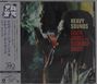 "HEAVY SOUNDS" steht in weißer und roter Schrift. Zwei Menschen, einer raucht, in gedämpftem Licht. Jazz-Atmosphäre.