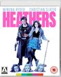 "HEATHERS" in großen pinken Buchstaben, darunter zwei Personen, eine mit einem Gewehr, die andere in blauer Kleidung.
