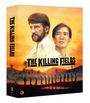 „THE KILLING FIELDS“, zwei Männer vor einem orangefarbenen Himmel, im Hintergrund eine Reihe von Personen und Palmen.