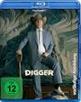 „DIGGER“, „FSK ab 12 freigegeben“, „vorläufige Abbildung“. Ein Mann im Anzug mit Cowboyhut posiert mit Schaufel.
