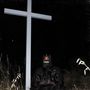 Unbekannte Schriftzeichen auf Gesichtsmaske. Dunkle Nacht, große Kreuz-Silhouette und maskierte Person in schwarzer Kleidung.