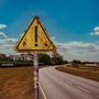 "James Marriott", "Warning Signs". Ein altes, dreckiges gelbes Warnschild vor einer Landstraße und blauem Himmel.