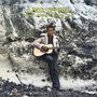 „LABI SIFFRE CRYING LAUGHING LOVING LYING“ in Gelb. Eine Person sitzt mit Gitarre vor einer steinigen Hintergrundkulisse.