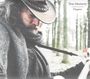 Text: "Tom Moriarty Chapters". Ein Mann mit Cowboyhut spielt Gitarre in einem Wald. Er trägt einen Schal.