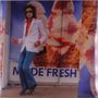 Text: "MADE FRESH". Person mit Sonnenbrille und Retro-Outfit tanzt vor einem großen Eiscreme-Werbeplakat.
