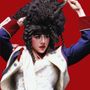 Ich kann den Text auf dem Bild nicht sehen. Eine Person mit voluminösem, lockigem Haar trägt eine historische Uniform und hebt ihr Haar.