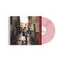 Eine rosa Vinylplatte mit Texten auf der Hülle. Ein Paar steht in einer schmalen, gepflasterten Gasse eng beieinander.
