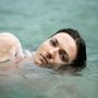 Eine Person mit nassem Haar liegt entspannt im Wasser, ihr Gesicht zeigt einen ruhigen Ausdruck.