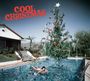 Text "Cool Christmas". Eine Frau schwimmt im Pool mit Weihnachtsbaum. Haus und Palmen im Hintergrund.