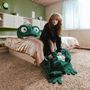 Kein Text sichtbar. 
Eine Person in einem Zimmer mit einem riesigen grünen Frosch-Plüsch auf dem Bett. Gemütliche Atmosphäre.