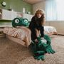 Eine Frau in einem Vintage-Zimmer sitzt auf einem riesigen grünen Plüschfrosch, der auf einem flauschigen Teppich liegt.