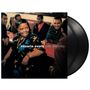 "cesaria evora café atlantico"; eine Frau in bunter Kleidung lacht mit mehreren Personen an einem Tisch. Vinyl im Hintergrund.