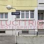 22. Falcogasse, LUCI TRIO ROTE SPRITZER. Straßenschild und Häuserfassade mit gelbem und grauem Anstrich.