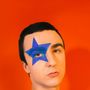 Eine Person mit einem blauen Stern im Gesicht vor orangenem Hintergrund.