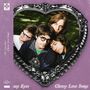 "The Lazy Eyes" und "Cheesy Love Songs" stehen auf einem lila Hintergrund. Vier Personen in einem herzförmigen Rahmen.