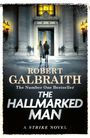 Text: "Robert Galbraith, The Number One Bestseller, The Hallmarked Man, A Strike Novel."  
Zwei Personen betreten ein beleuchtetes Gebäude.