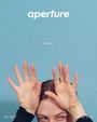 „aperture“, „Secrets“, „No. 263“, „Summer 2026“. Ein Gesicht mit hochgehobenen Händen vor blauem Hintergrund.