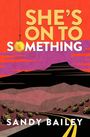 Text: "SHE'S ON TO SOMETHING" und "SANDY BAILEY".   
Eine orangefarbene und violette Landschaft mit Straße.