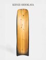 Text "KENZI SHIOKAVA" über einem länglichen, hölzernen Kunstobjekt in natürlichen Tönen und schwarzem Rand.