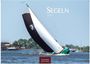 "Segeln 2027" oben, "CASARES EDITION" unten. Ein Segelboot neigt sich im Wind auf dem Wasser, Zuschauer am Ufer.