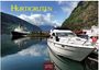 Hurtigruten, 2024, Casares Edition. Ein Kreuzfahrtschiff und eine Yacht, umgeben von Bergen und ruhigem Wasser.