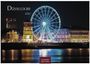 „Düsseldorf 2027“. Ein beleuchtetes Riesenrad in der Nacht, umgeben von historischen Gebäuden am Flussufer.