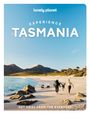 „EXPERIENCE TASMANIA“, ein Paar schwingt ein Kind an einem Strand, Berge im Hintergrund, blauer Himmel.