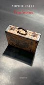 "SOPHIE CALLE, True Stories, ACTES SUD". Ein alter, abgenutzter Koffer auf einem grauen Boden, von Licht beschienen.