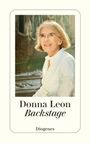"Donna Leon, Backstage, Diogenes". Eine Frau mit grauem Haar und Brille trägt ein weißes Hemd und lächelt. Hintergrund: Stadt.
