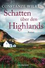 „Schatten über den Highlands“ von Constanze Wilken. Ein weißes Haus, grüne Hügel und zwei Pferde im Vordergrund.