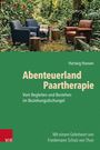 "Abenteuerland Paartherapie" von Hartwig Hansen. Zwei Stühle im Wald, Tische aus Baumstümpfen, Tuch auf einem Stuhl.