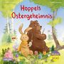 Text: Hoppels Ostergeheimnis. Ein Hase und ein Bär bemalen im Freien Ostereier, umgeben von Bäumen und Blumen.