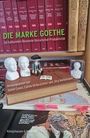 „DIE MARKE GOETHE“ auf einem Buchrücken in einem Regal; daneben Büsten und Figuren auf Büchern.