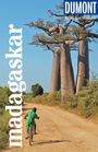 „madagaskar“ und „DUMONT Reise-Taschenbuch“. Ein Kind fährt auf einem sandigen Weg mit dem Fahrrad an großen Baobab-Bäumen vorbei.