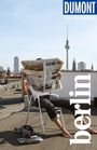 Texte: Dumont Reise-Taschenbuch, berlin. Eine Person liest eine Zeitung auf einem Dach, im Hintergrund der Berliner Fernsehturm.