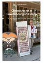 Eine lächelnde Person hält ein langes Dokument, daneben eine Figur mit Strohhut. Text: "Chronicles of a Luxembourgish Henro".