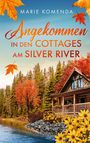 Oben steht "Marie Komenda". Darunter: "Angekommen in den Cottages am Silver River". Darunter: "Roman". Eine herbstliche Hütte am Fluss.