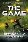 Text: "Christian Tielmann", "THE GAME", "Gefangen im Labyrinth". Zwei Figuren springen in einem grünlichen, futuristischen Raum.