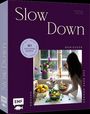 "Slow Down" - Ein Buch über Soulfood-Rezepte; eine Frau kocht in einer gemütlichen Küche mit frischem Obst und Blumen.