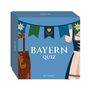 Text: "BAYERN QUIZ". Illustration eines blauen Kastens mit Lederhose und Dirndl, sowie Blumen und Wimpeln.