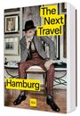 "GU, The Next Travel Hamburg." Ein älterer Mann in Anzug und Hut sitzt auf einem Stuhl vor gerahmten Bildern.