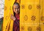 Ein Mönch schaut hinter einem gelben Vorhang mit bunten Mustern hervor. Texte: "Eva-Maria Fahrner-Tutsek", "THE MONK AND THE TIGER", "Postcards from Bhutan".