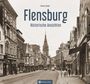 Flensburg: Historische Ansicht einer alten Straße mit Geschäften und einer Kirche im Hintergrund, voller Menschen und Schilder.